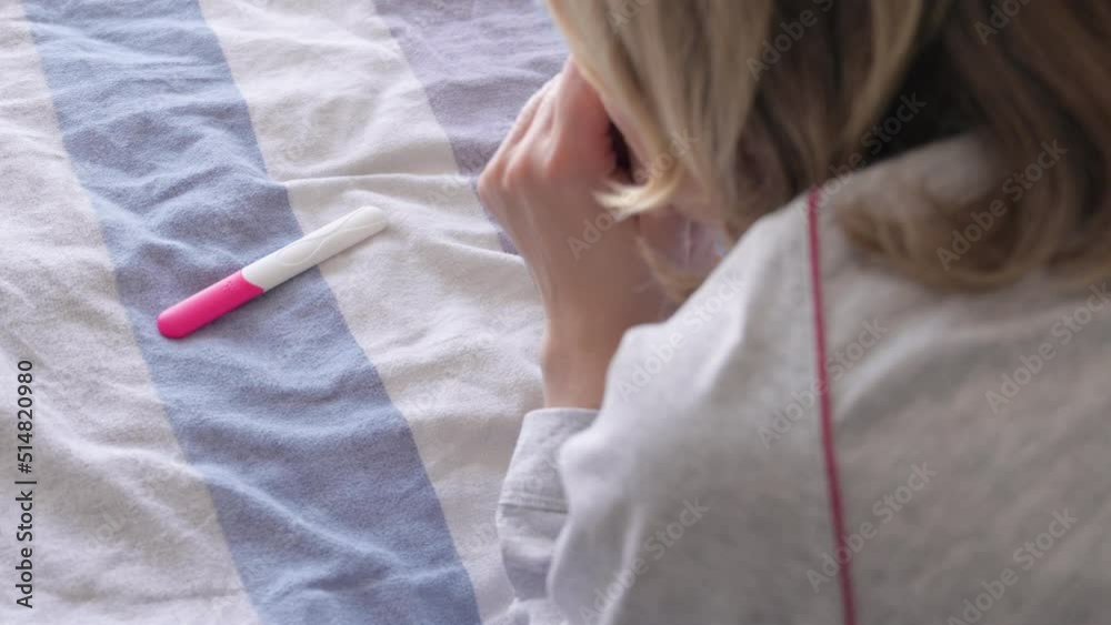 Happy woman lying in bed and making pregnancy test. Unrecognizable girl