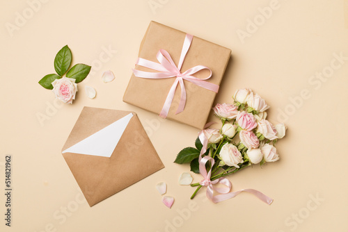 Envelope, gift box and rose flowers on color background, top view