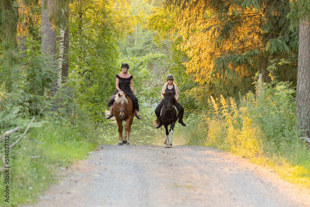 Two riders coming up hill during sunset. The sun is shining from behind. Female riders have have black helmets. Two riders coming up hill during sunset. The sun is shining from behind. Female riders have have black helmets.