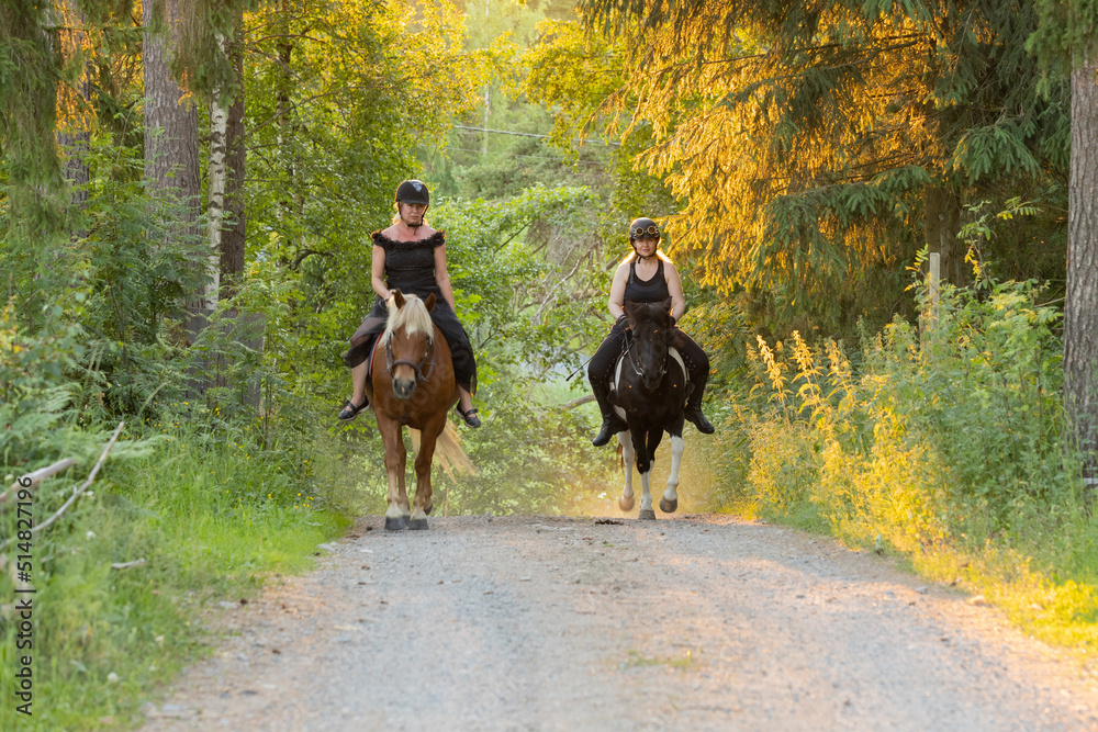 Two riders coming up hill during sunset. The sun is shining from behind. Female riders have have black helmets. Two riders coming up hill during sunset. The sun is shining from behind. Female riders have have black helmets.