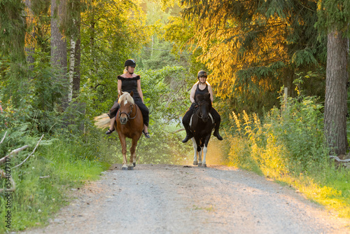 Two riders coming up hill during sunset. The sun is shining from behind. Female riders have have black helmets. © AnttiJussi
