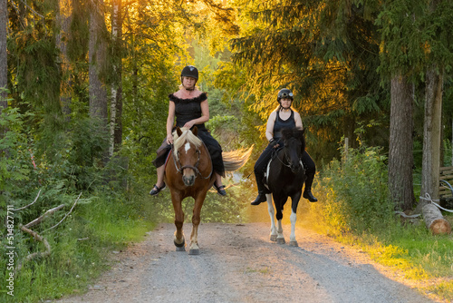 Two riders coming up hill during sunset. The sun is shining from behind. Female riders have have black helmets.