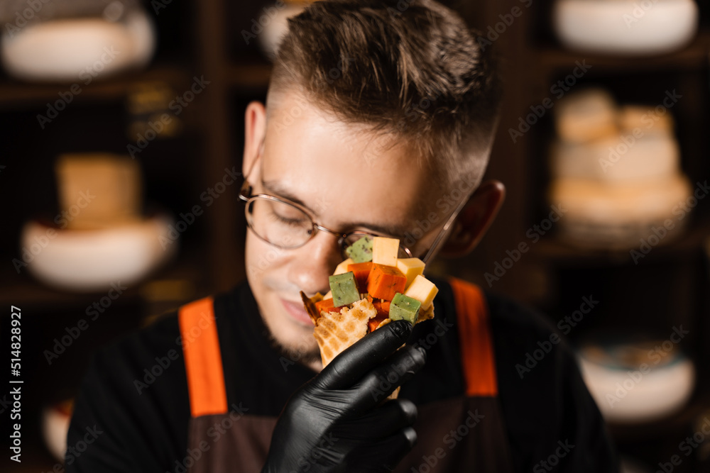Creative photo of mix of cheeses in waffle cup. Handsome man with mix of young Gouda, young goat, lavander cheese, green and red pesto in waffle cup. Creative idea for advertising a cheese shop.
