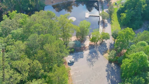 aerial footage of a gorgeous summer landscape in the park with a lake and brown wooden bridge surrounded by lush green trees with parked cars, a playground and a water fountain in the lake photo