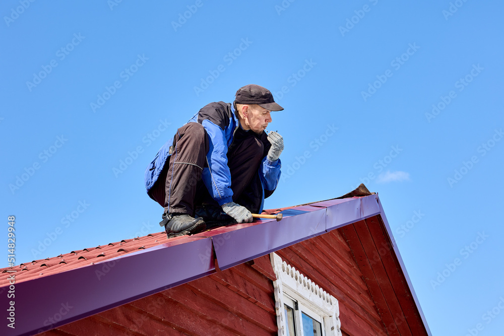 Nailing into tin roof while roofing, worker uses hammer to fix roof. Nailing into tin roof while roofing, worker uses hammer to fix roof.