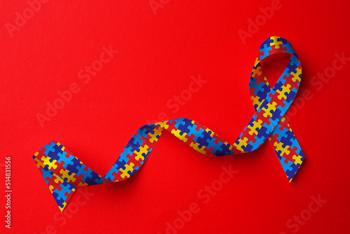 World Autism Awareness Day. Colorful puzzle ribbon on red background, top view