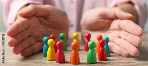 Woman protecting colorful pawns at wooden table, closeup. Diversity and Inclusion concept
