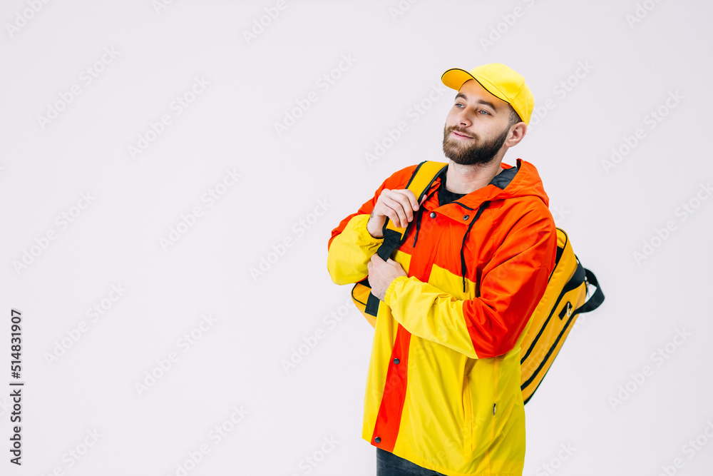 Young bearded delivery man wearing red yellow uniform and cap in studio on white background. Copy space Young bearded delivery man wearing red yellow uniform and cap in studio on white background. Copy space