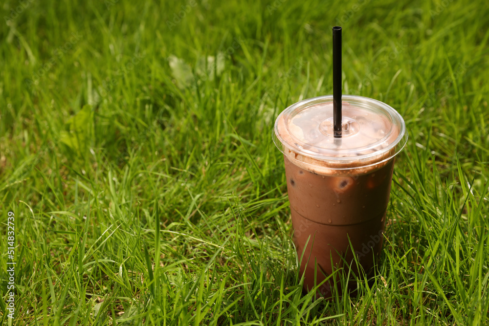Takeaway plastic cup with cold coffee drink and straw on green grass outdoors, space for text Takeaway plastic cup with cold coffee drink and straw on green grass outdoors, space for text