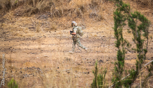 A soldier runs across the field in the hands of a machine gun. Airsoft game. A guy in a military uniform runs through the field