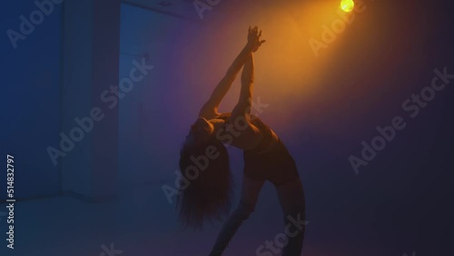 Beautiful graceful girl dancing in colorful studio light in smoke at night. Modern dance, slow motion, handheld video