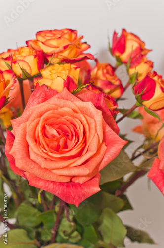 top  front view  medium and close distance of  a ceramic  colorful  vase  with three  long stemmed  orange  roses and a dozen  baby  orange and red roses  in full bloom