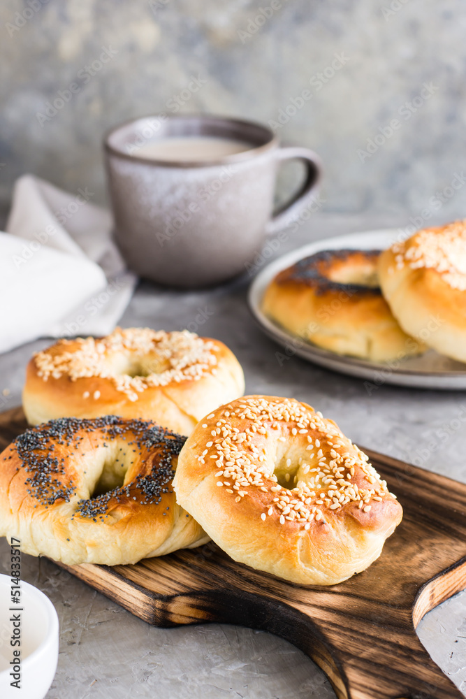 Bagels with poppy seeds and sesame seeds on a plate and a cup of coffee on the table. Vertical view