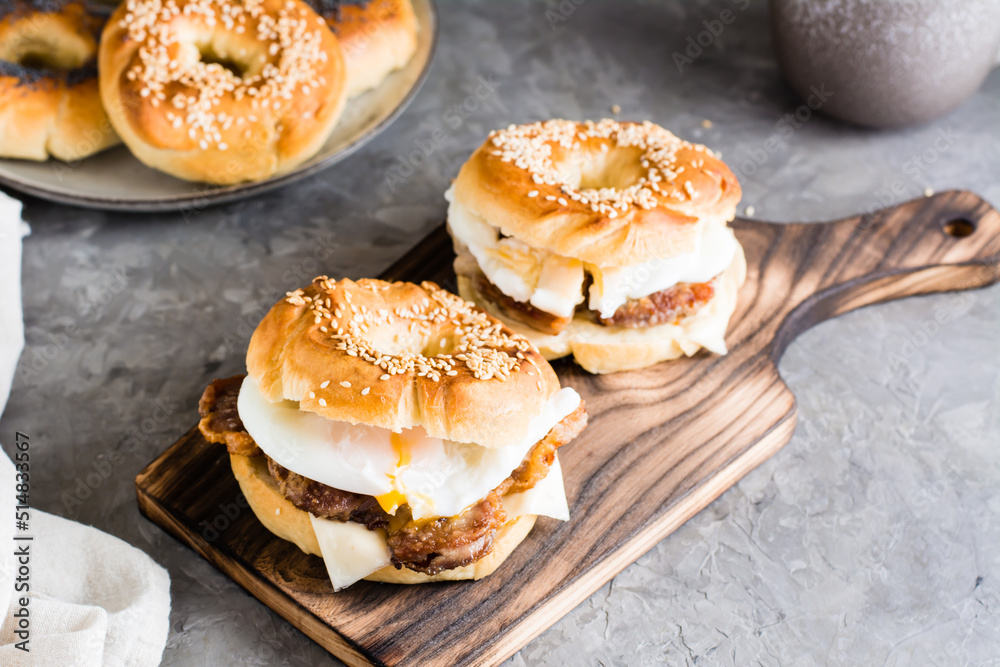Bagels sandwiches with cheese, fried meat and poached egg on a board. Homemade fast food
