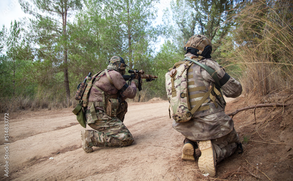 Two military men with weapons from the back. Military men sit on their knees and discuss battle tactics. Airsoft team game