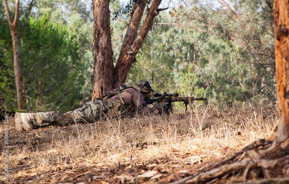 A sniper with a weapon in his hands lies on the ground. A military man aims through the scope of a sniper rifle. A man in camouflage lies on the ground