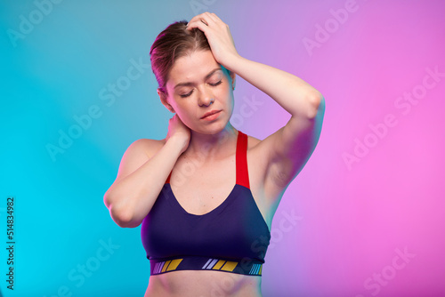 Woman headache pain with eyes closed. Girl in sportswear. Female fitness portrait isolated on neon pink blue color background.