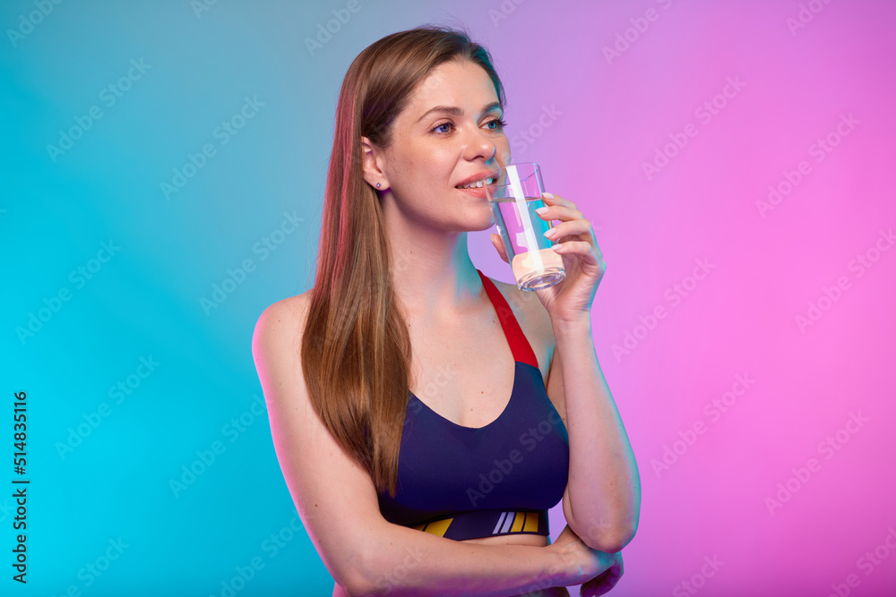 Smiling sporty woman in sportswear drinking water and looking away. Female fitness portrait isolated on neon multicolor background. Smiling sporty woman in sportswear drinking water and looking away. Female fitness portrait isolated on neon multicolor background.