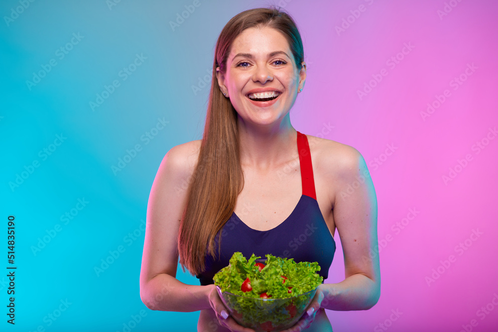 Smiling sporty woman in sportswear holding green salad in glass bowl in front of her. Female fitness portrait isolated on neon multicolor background. Smiling sporty woman in sportswear holding green salad in glass bowl in front of her. Female fitness portrait isolated on neon multicolor background.