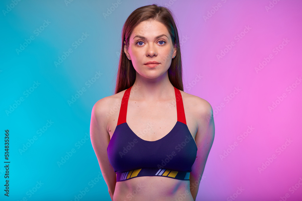 Fototapeta premium Serious sporty woman in fitness bra sportswear with hands behind back. Female fitness portrait isolated on neon colored background.