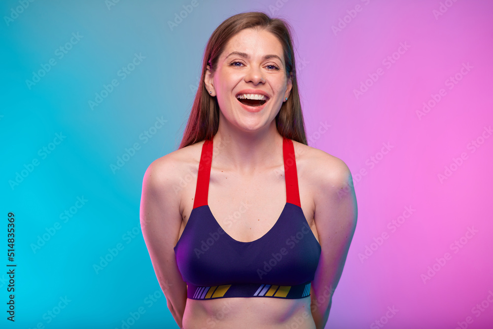 Happy mouth open sporty woman in fitness bra sportswear with hands behind back. Female fitness portrait isolated on neon colored background.