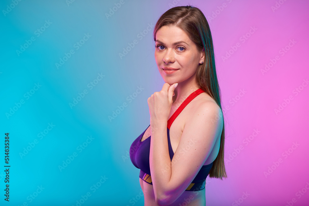 Obraz premium Thinking smiling sporty woman in fitness bra sportswear profile view. Female fitness portrait isolated on neon multicolor background. Girl face with hand touching chin.
