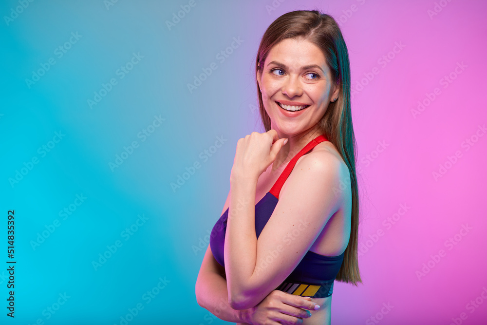 Thinking smiling sporty woman in fitness bra sportswear profile view, looking back over shoulder. Female fitness portrait isolated on neon multicolor background. Girl face with hand touching chin.