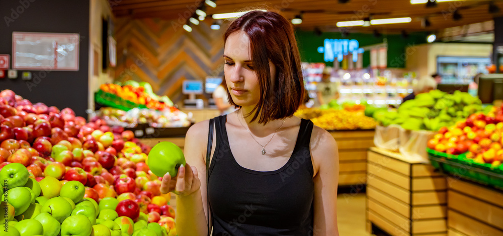 Woman in a supermarket at the shelf for fruits shopping apple