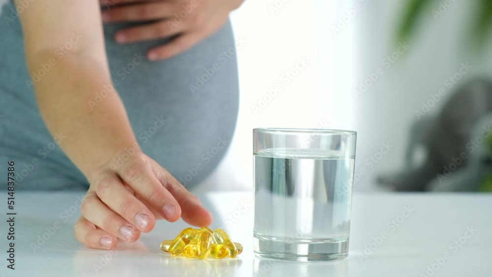 Omega DHA capsules and glass of water and pregnant woman at home