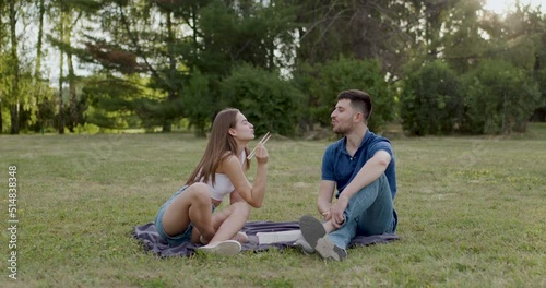 at a picnic, a woman dressed in white feeds her boyfriend or dressed in blue with sushi with chopsticks photo