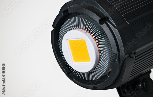 Yellow LED module in photographic reflector with aluminum cooling fins on white background. Detail of black high-power electric light source from semiconductor diodes with metal heatsink. Photography. photo