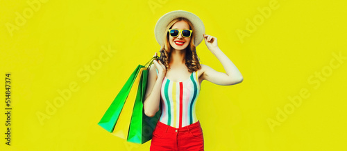 Portrait of beautiful happy smiling young woman with colorful shopping bags wearing summer straw hat on yellow background