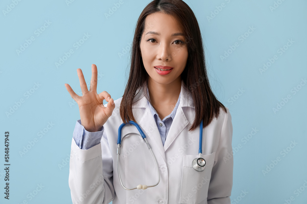 Female Asian doctor showing OK on blue background Female Asian doctor showing OK on blue background
