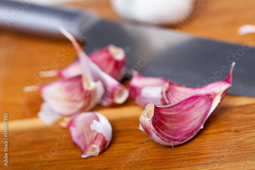 Fresh garlic cloves on wooden table with kitchen knife. Cooking food concept.