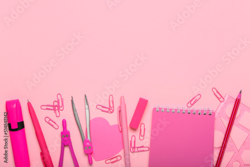 Pink paper clips with stationery supplies on color background