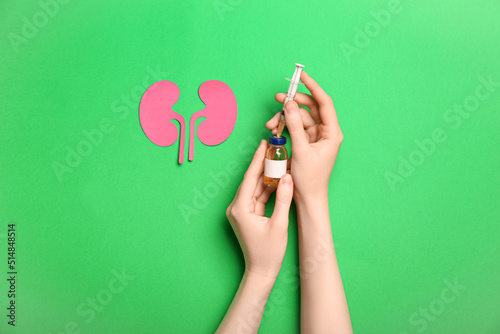 Woman with ampule, syringe and paper kidneys on green background photo