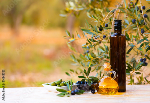 Fresh olives in salad bowls and oil in glass decanter and bottles on wooden table under branches of olive tree.. photo