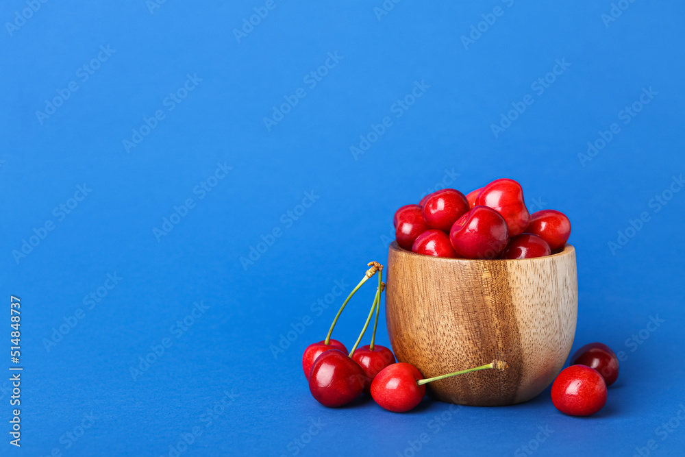 Wooden bowl with sweet cherries on blue background