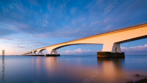 A long bridge over the sea during sunset. Long exposure photo. Landscape during a bright sundown. The sea and the bridge. Zeeland bridge, Netherlands.