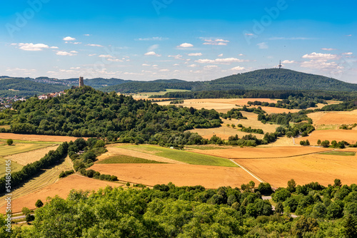 Panoramafoto vom Bergfried der Höhenburg Vetzberg auf einem Vulkanberg in Mittelhessen, eingebettet in eine landwirtschaftlich genutzte Landschaft mit leicht bewölktem Himmel am Horizont und dem Dünsb