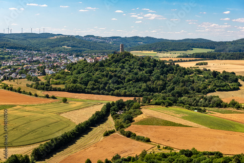 Der Bergfried der Höhenburg Vetzberg auf einem Vulkanberg in Mittelhessen, eingebettet in eine landwirtschaftlich genutzte Landschaft mit leicht bewölktem Himmel am Horizont bei schönem Sommerwetter