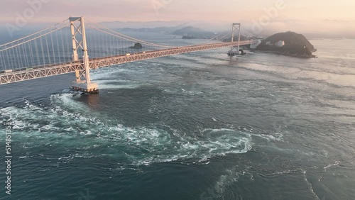 Aerial: Pullback on whirlpools under Naruto suspension bridge at sunset