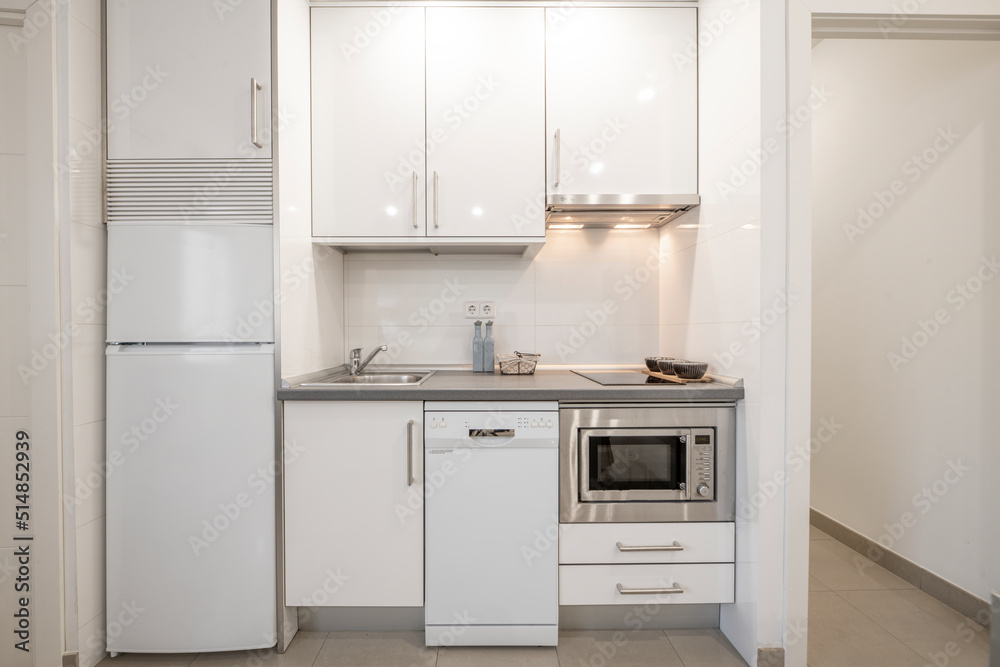 Small kitchen front with white furniture and integrated appliances, gray countertop and gray stoneware floors Small kitchen front with white furniture and integrated appliances, gray countertop and gray stoneware floors