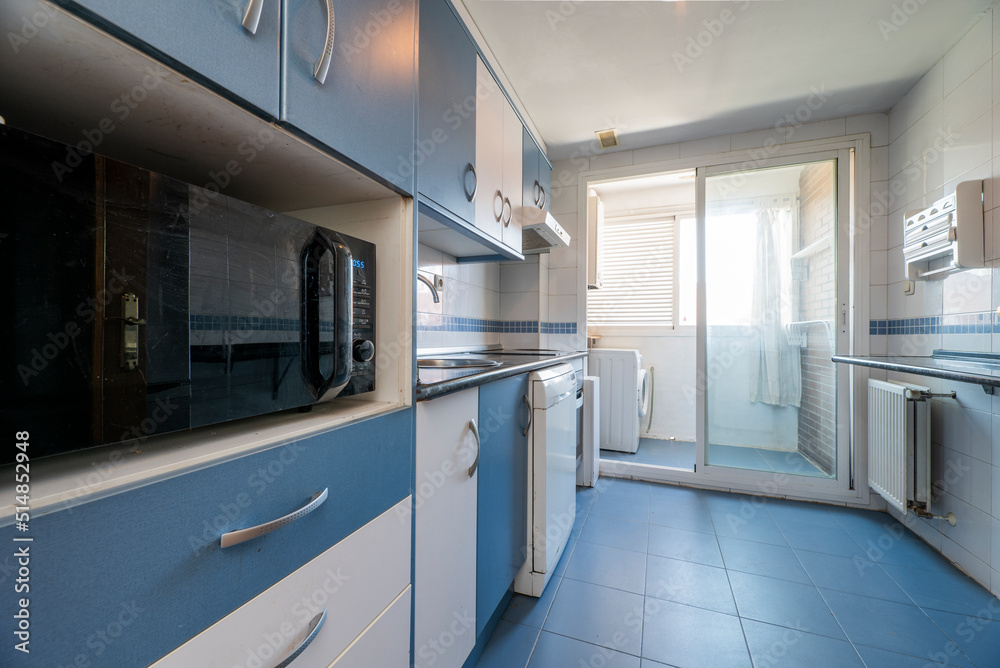 In front of a kitchen with white and blue furniture, built-in appliances, drawers and column with furniture and black microwave oven with blue stoneware floors In front of a kitchen with white and blue furniture, built-in appliances, drawers and column with furniture and black microwave oven with blue stoneware floors
