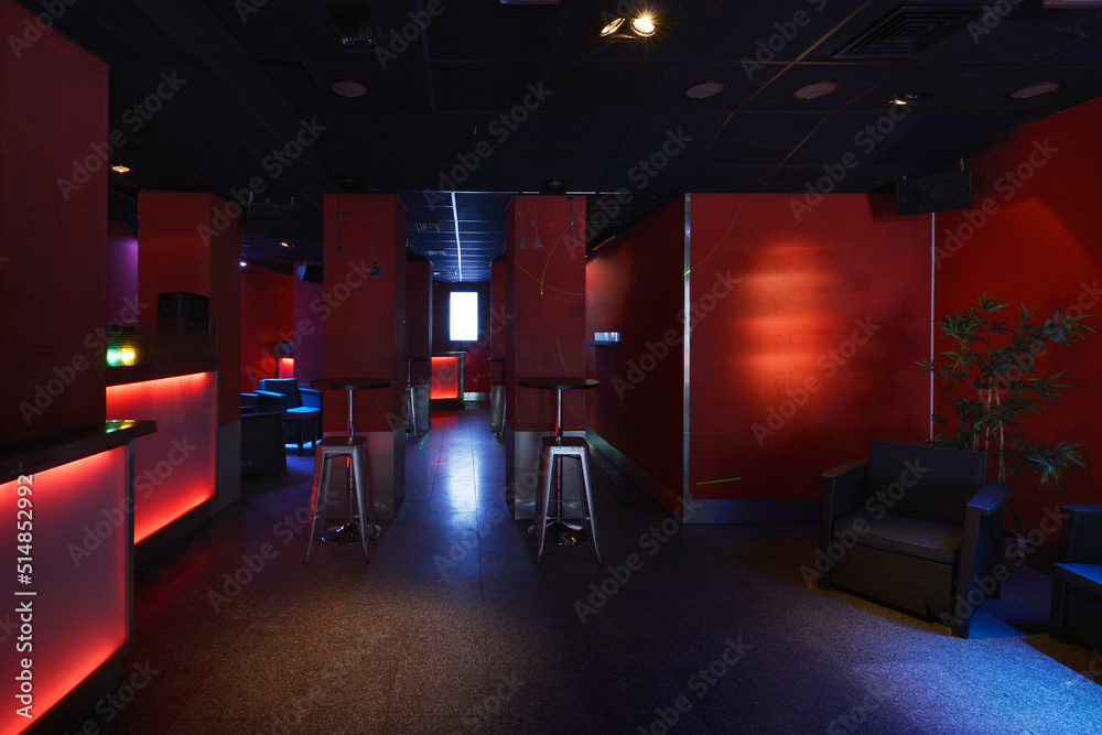 Lounge with high round tables with metal stools and individual chairs with red and neon walls in a cocktail bar