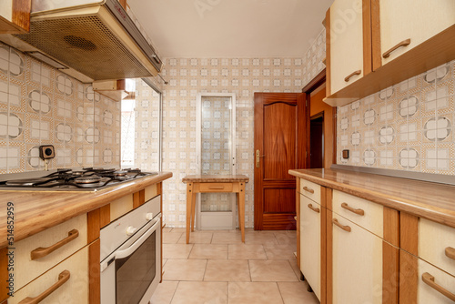 Kitchen with old wooden furniture on both sides of the wall and kitsch vintage cream tiles and stoneware floors, wooden table and reddish carpentry