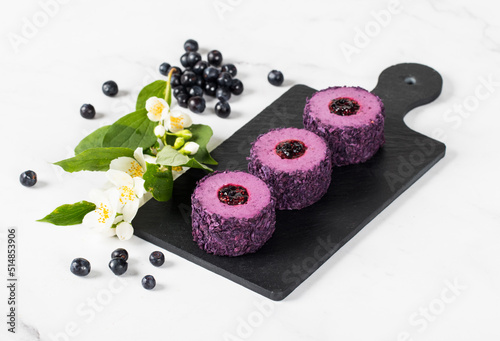 Mousse blueberry chocolate cream dessert, in the form of round sweet sushi, on a serving board. Light background	