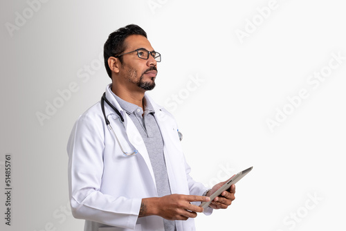 doctor, man holding tablet looks up distantly, wearing white uniform and stethoscope, white background