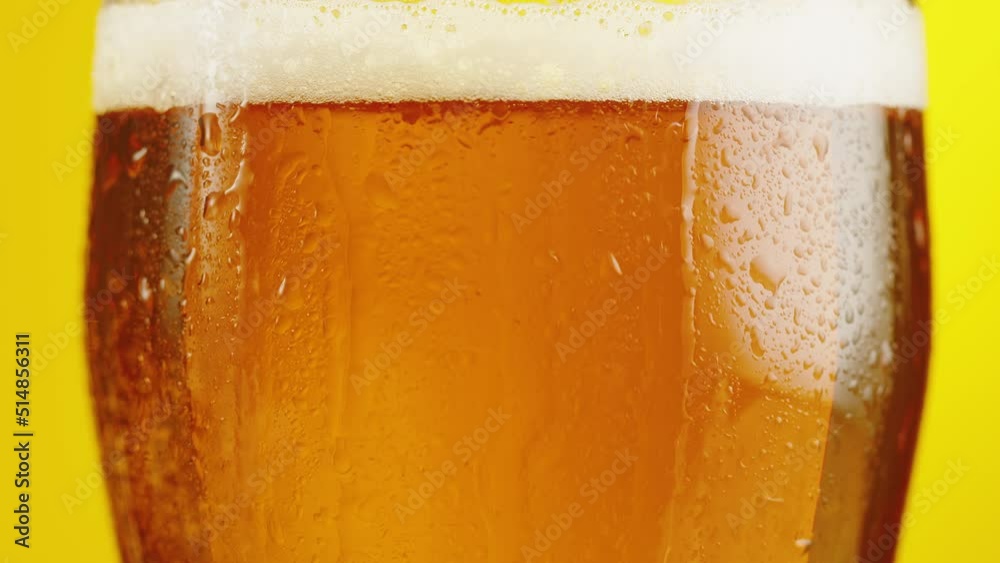 Foamy beer in glass close-up. Alcohol golden beer drink in mug. Fresh pale ale on yellow background. 