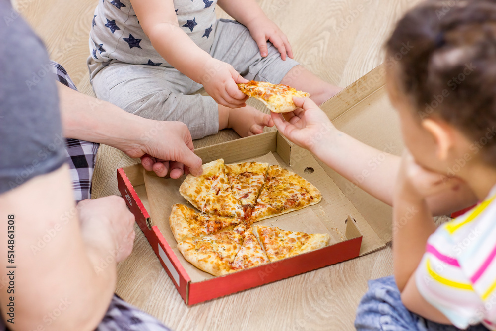 Family hands taking pizza slices on wooden floor background.